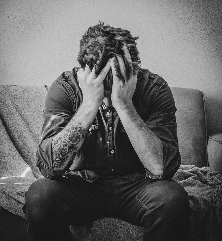 Hombre sentado en un sillón, con las manos en la cara y . Visibilizar y desmitificar el suicidio. Asoc. Papageno