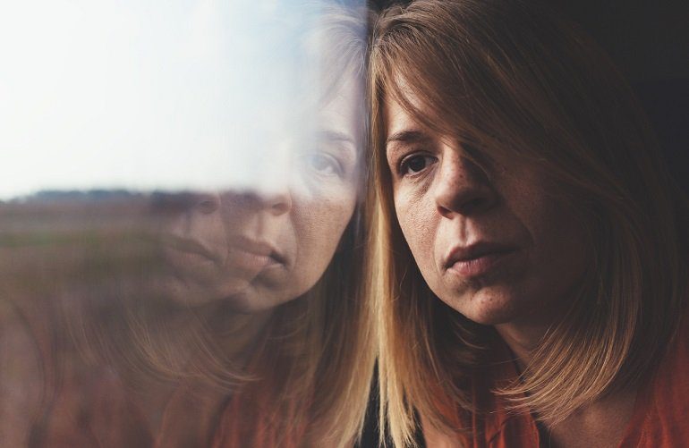Mujer con cara triste pegada a un cristal. Visibilizar y desmitificar el suicidio. Asoc. Papageno.